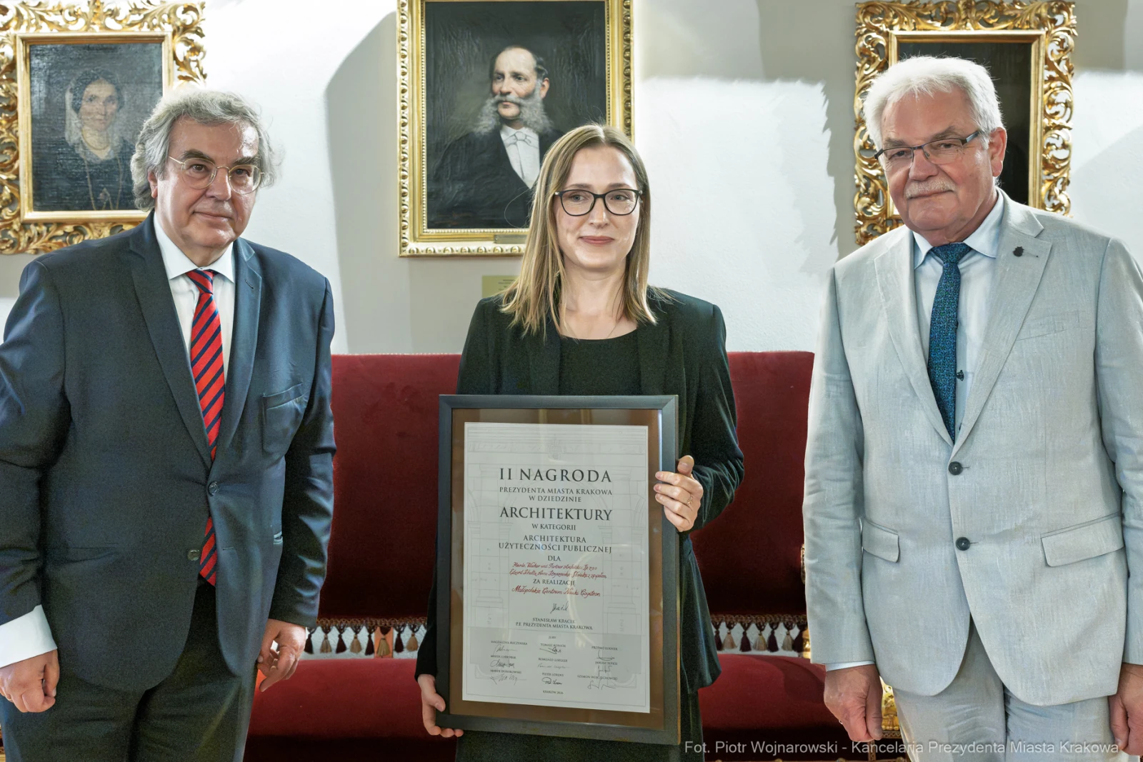 Kobieta trzymająca dyplom nagrody architektonicznej, obok dwóch mężczyzn w garniturach.  Autor: Piotr Wojnarowski
