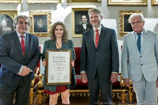 Wręczenie III nagrody architektonicznej w eleganckim otoczeniu. Cztery osoby z dyplomem.