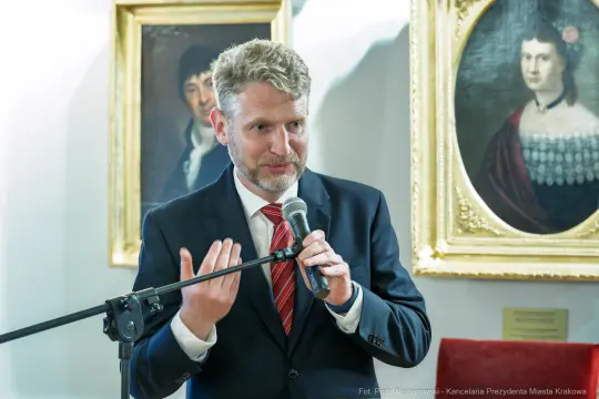 Mężczyzna w garniturze przemawia do zgromadzonej publiczności.
