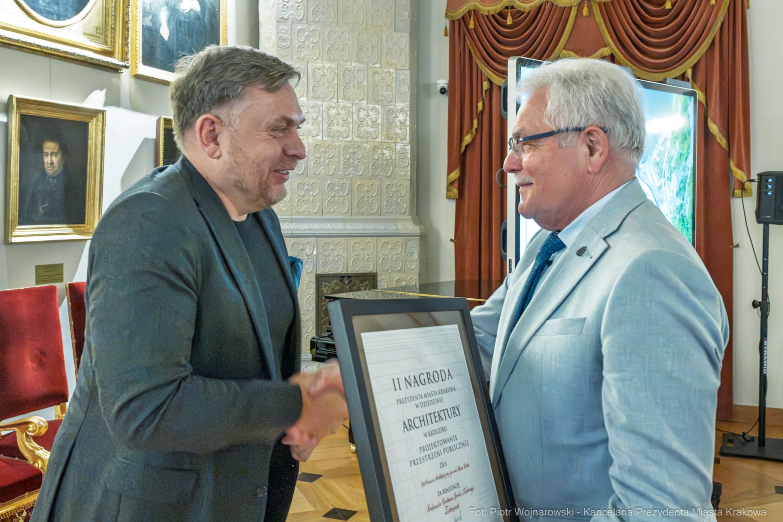 Mężczyźni uścisną ręce, jeden wręcza drugiemu dyplom nagrody za osiągnięcia w architekturze.  Autor: Piotr Wojnarowski
