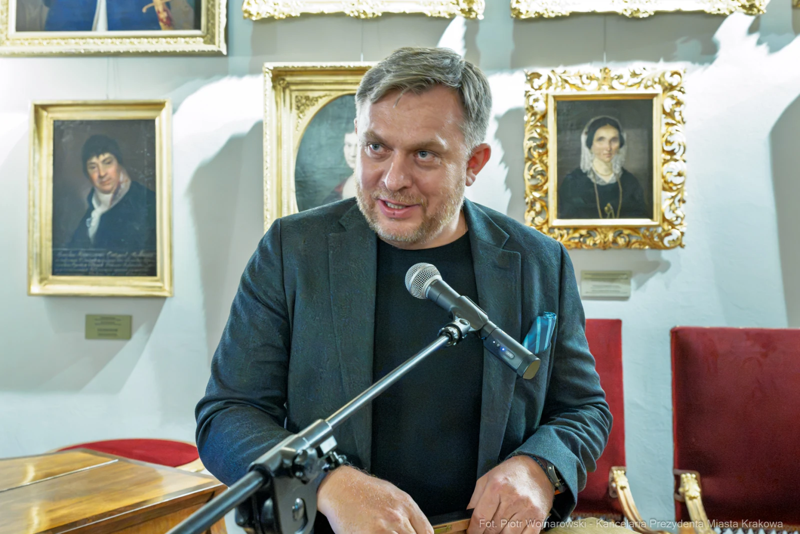 Mężczyzna przemawia przy mikrofonie, w tle portrety na ścianie.  Autor: Piotr Wojnarowski