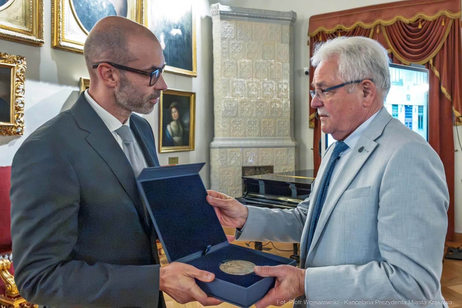 Dwaj mężczyźni wymieniają się medalem w eleganckim wnętrzu.  Autor: Piotr Wojnarowski