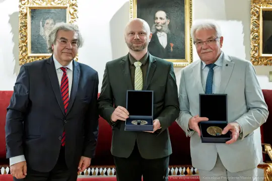 Trzej mężczyźni trzymają medale w eleganckim wnętrzu.