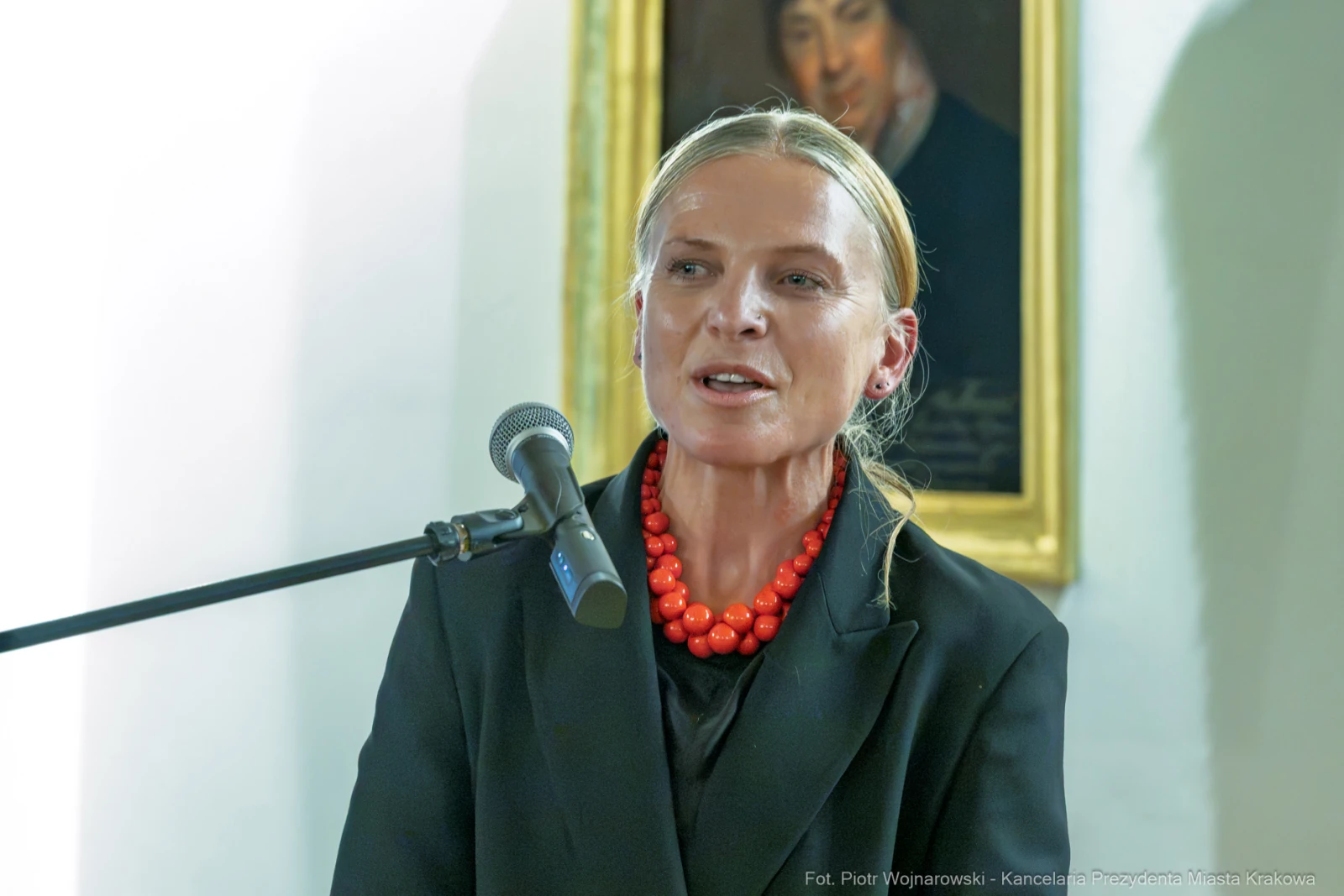 Kobieta w czarnym stroju z czerwonymi koralikami przemawia przy mikrofonie.  Autor: Piotr Wojnarowski