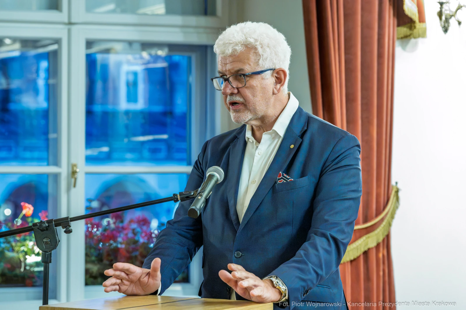 Mężczyzna w garniturze przemawia przy mikrofonie w eleganckim wnętrzu.  Autor: Piotr Wojnarowski
