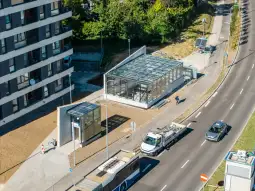 Nowoczesny przystanek autobusowy z przeszkloną konstrukcją obok ruchliwej ulicy.