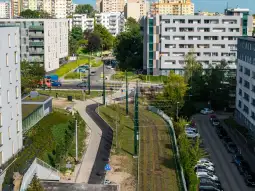 Widok na nowoczesne osiedle z zielenią, torami kolejowymi i ulicą.