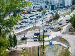 Widok na parking, torowisko tramwajowe i ruch uliczny w miejskim otoczeniu.