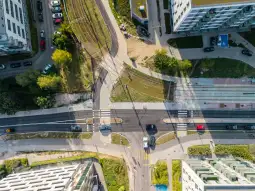 Widok z góry na skrzyżowanie dróg z torami tramwajowymi i otaczającą zabudową.