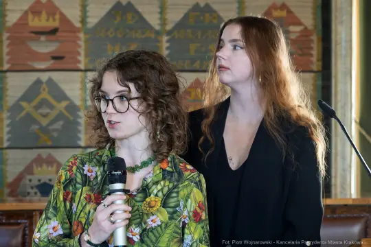 Dwie kobiety przemawiają na konferencji, jedna trzyma mikrofon.