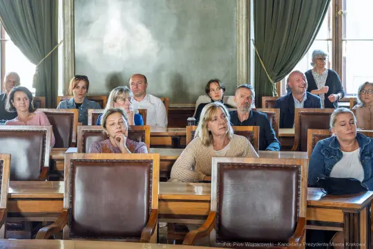Grupa osób siedzących w sali obrad, skupionych na prezentacji.