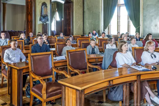 Grupa ludzi siedzących w sali konferencyjnej, słuchających wykładu.