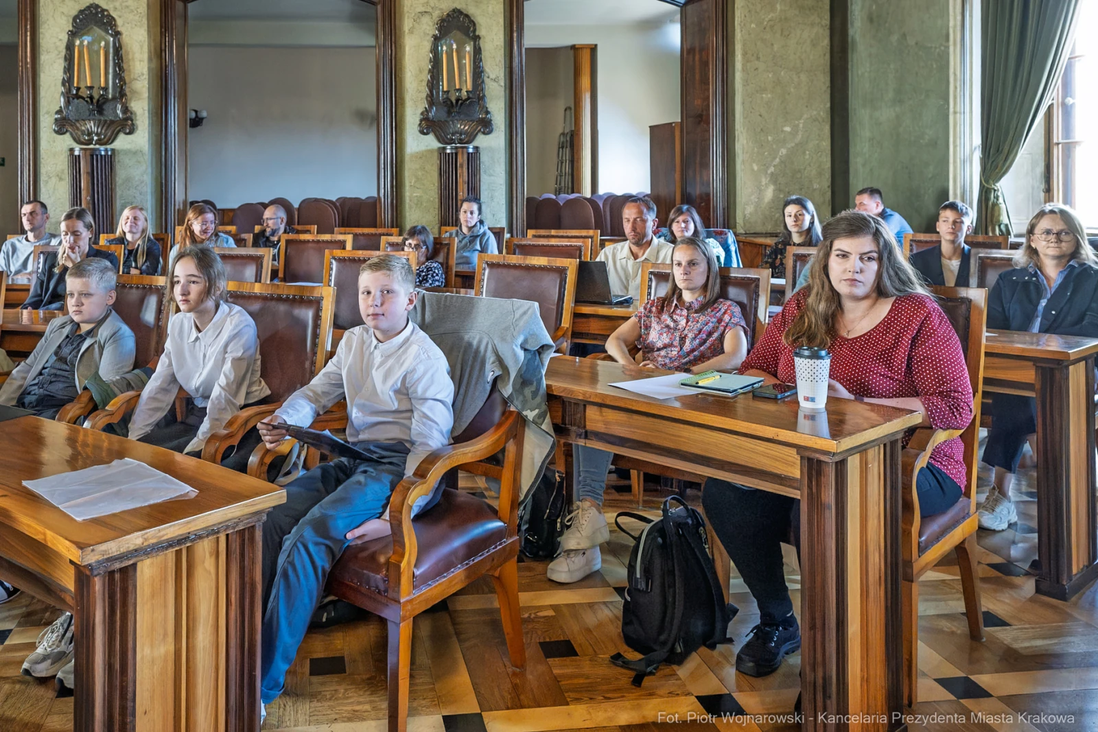 Grupa dzieci i dorosłych siedzących w sali, uczestniczących w spotkaniu.  Autor: Piotr Wojnarowski