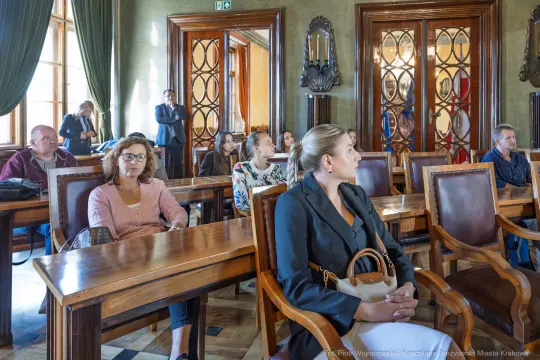Grupa ludzi siedzących w sali, zwróconych w stronę prelegenta.