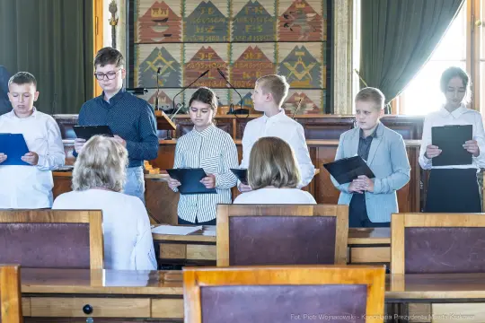 Grupa dzieci w strojach formalnych podczas uroczystości w sali obrad.