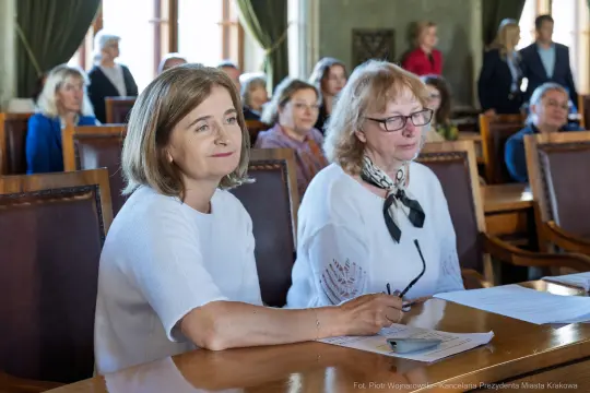 Dwie kobiety siedzące przy stole, uczestniczące w spotkaniu w sali konferencyjnej.