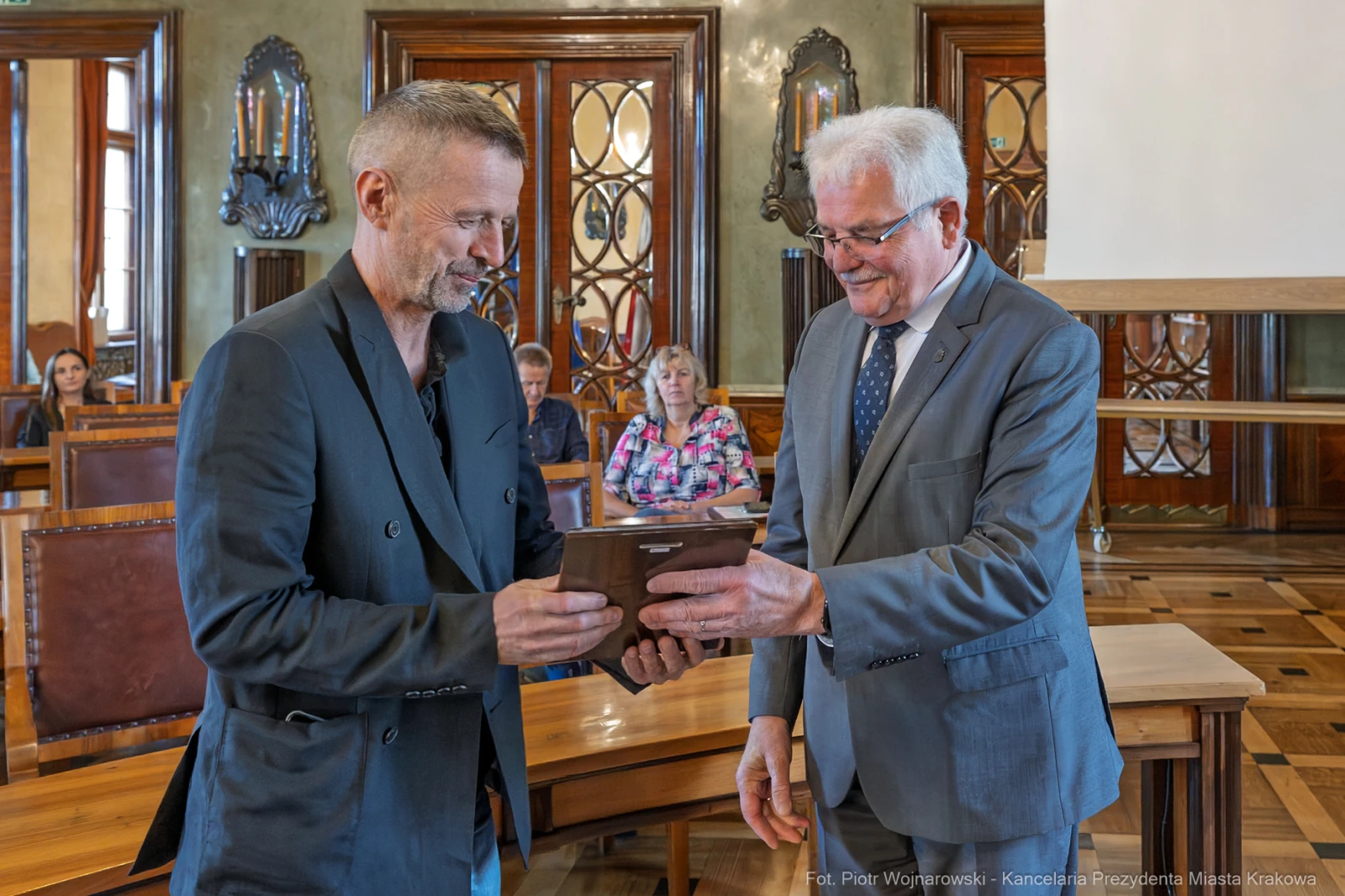 Mężczyźni wręczają sobie nagrodę w eleganckim wnętrzu z drewnianymi meblami.  Autor: Piotr Wojnarowski