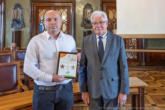 Mężczyzna wręczający nagrodę drugiemu mężczyźnie w eleganckim wnętrzu.