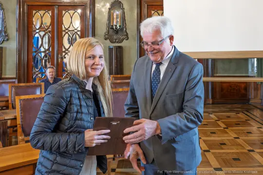 Wręczenie nagrody przez mężczyznę w garniturze kobiecie z uśmiechem w eleganckim wnętrzu.
