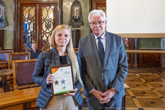 Kobieta z dyplomem i mężczyzna w garniturze w sali konferencyjnej.