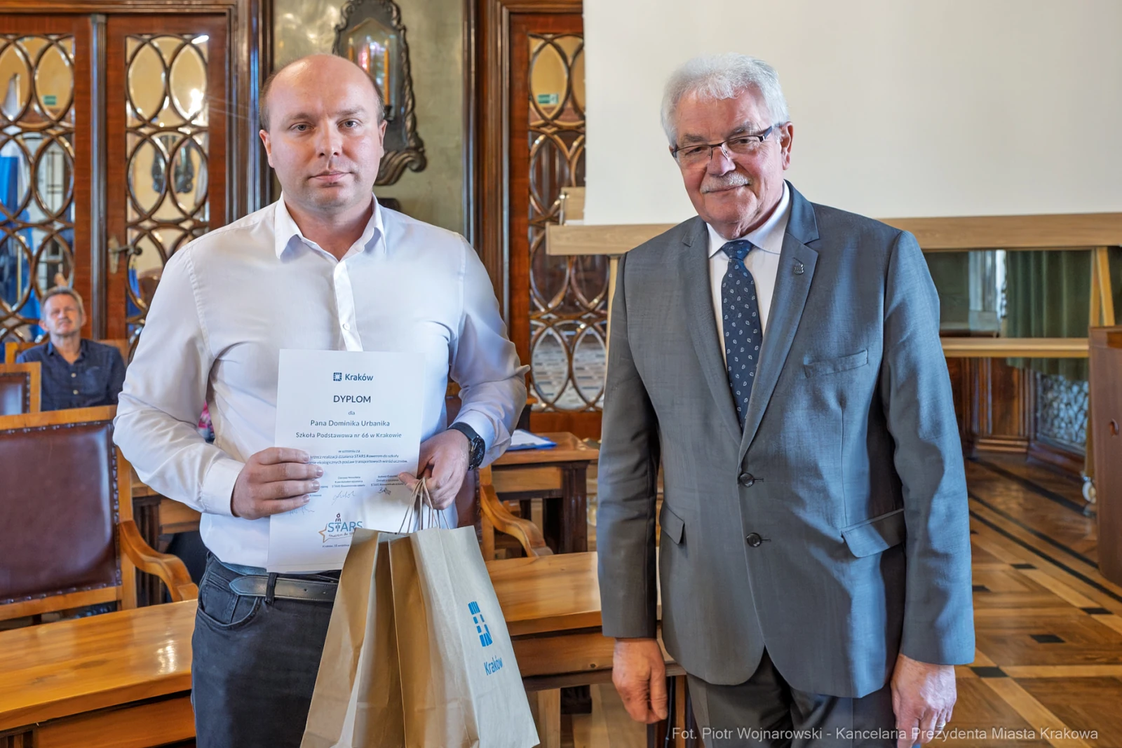 Mężczyzna trzyma dyplom i torbę, obok stoi starszy mężczyzna w garniturze.  Autor: Piotr Wojnarowski