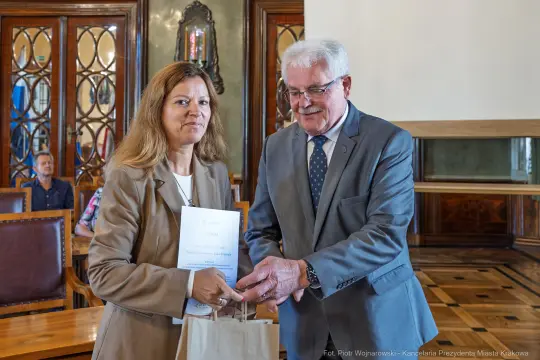 Wręczenie nagrody przez mężczyznę kobiecie w eleganckim wnętrzu.