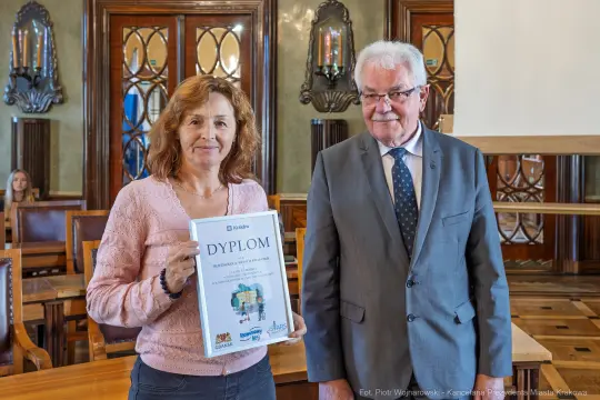 Kobieta trzyma dyplom, obok niej stoi mężczyzna w garniturze.