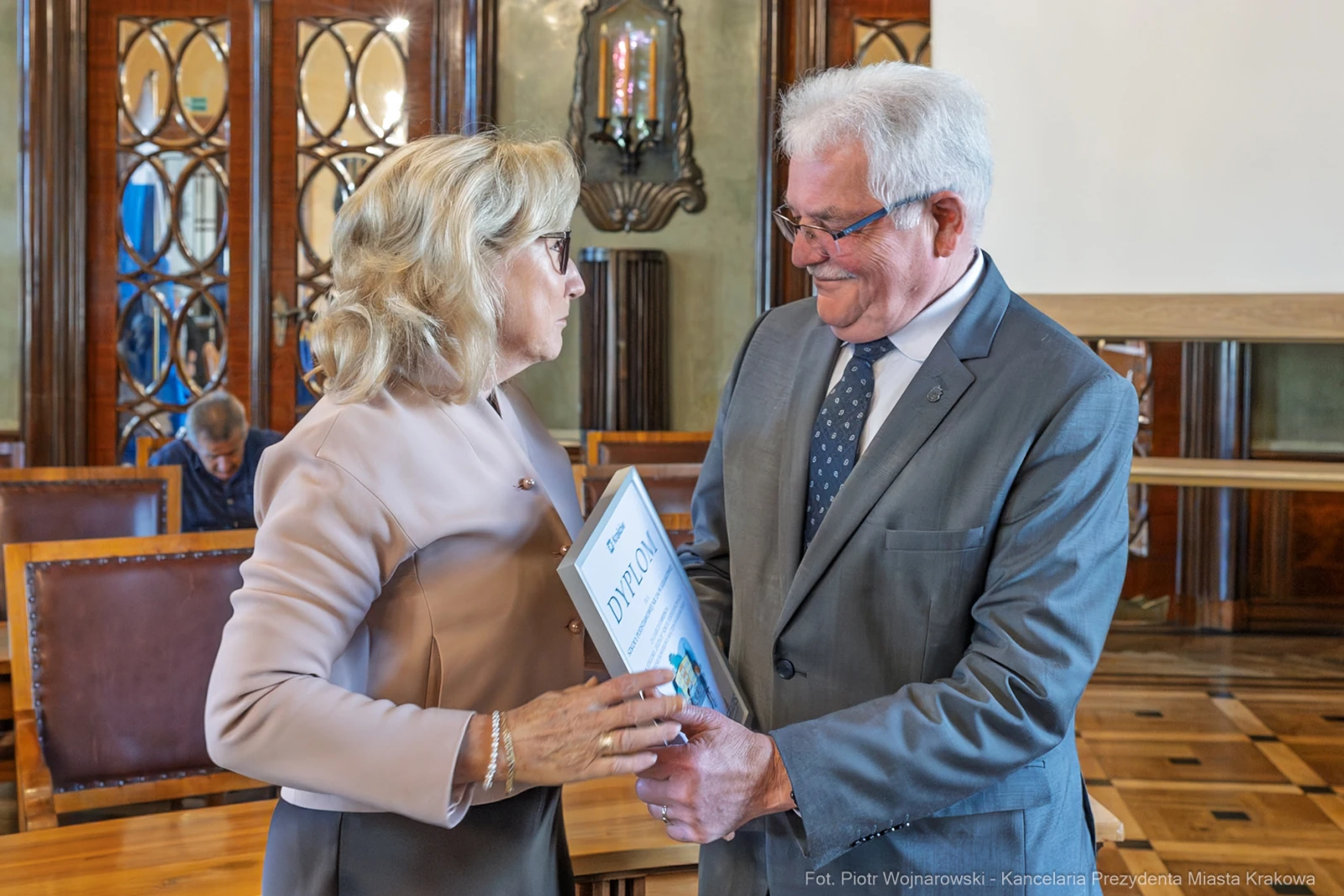 Wręczenie nagrody w eleganckim wnętrzu, uśmiechnięte osoby wymieniają się dokumentem.  Autor: Piotr Wojnarowski