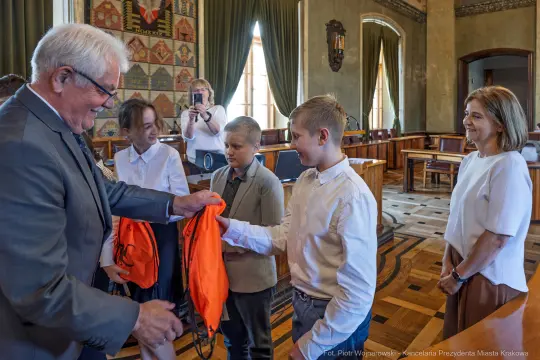 Wręczenie pomarańczowych kamizelek dzieciom w sali obrad.