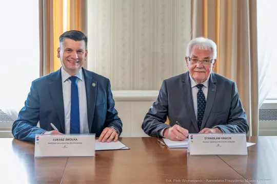Dwaj mężczyźni podpisują dokumenty przy stole.