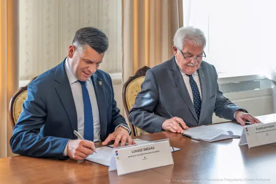 Dwaj mężczyźni podpisują dokumenty przy stole.