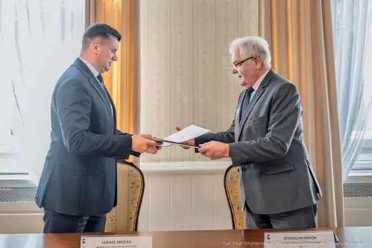 Dwaj mężczyźni wymieniają dokumenty podczas ceremonii podpisania umowy.