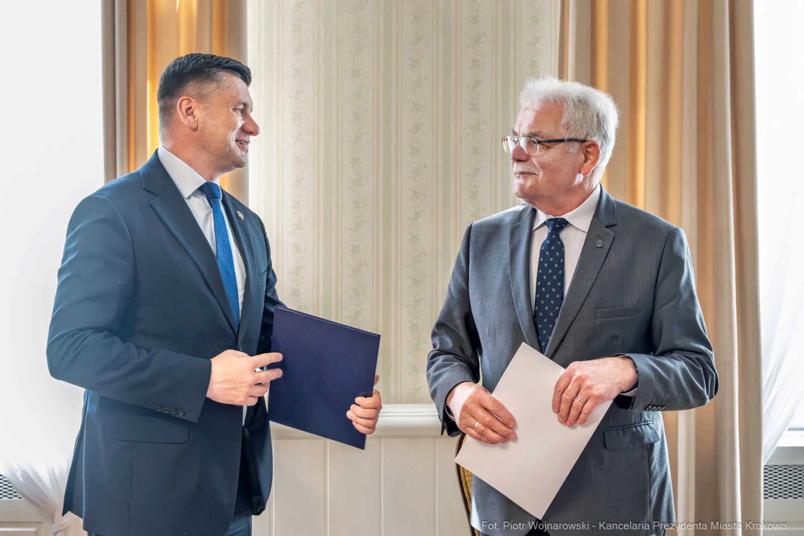 Dwaj mężczyźni w garniturach, rozmawiający i trzymający dokumenty.  Autor: Piotr Wojnarowski