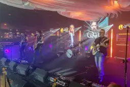 Zespół grający na scenie podczas festiwalu muzycznego, oświetlenie i sprzęt muzyczny w tle.