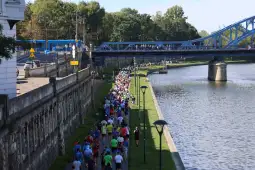Tłum biegaczy na ścieżce wzdłuż rzeki, most w tle.