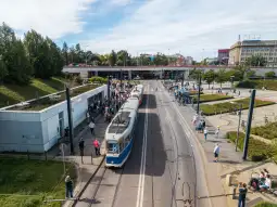 Tramwaj na przystanku z tłumem pasażerów i zielonym otoczeniem.