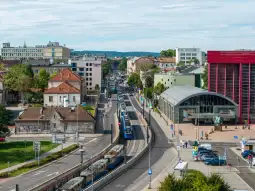 Widok na miasto z tramwajami, budynkami i zielenią w tle.
