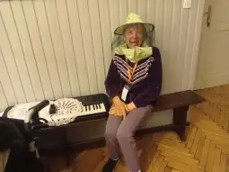 Starsza kobieta w kapeluszu z siatką, uśmiechająca się, siedzi obok keyboardu.