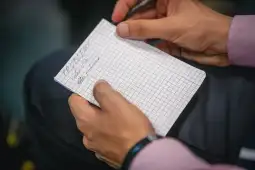 Osoba pisząca notatki w kratkowanym zeszycie.