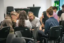 Grupa młodych ludzi w dyskusji w sali konferencyjnej.