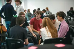 Grupa młodych ludzi rozmawia w sali konferencyjnej.