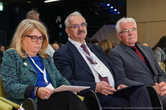 Trzy osoby siedzące na konferencji, skupione na notatkach.