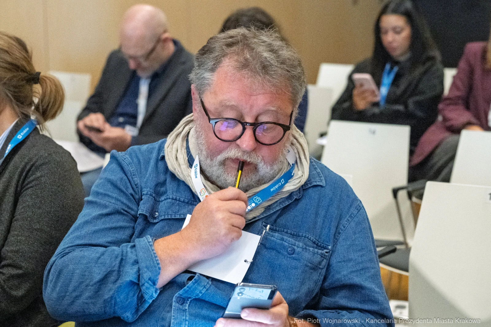 Mężczyzna z brodą pisze notatki, trzymając długopis i telefon w rękach.  Autor: Piotr Wojnarowski