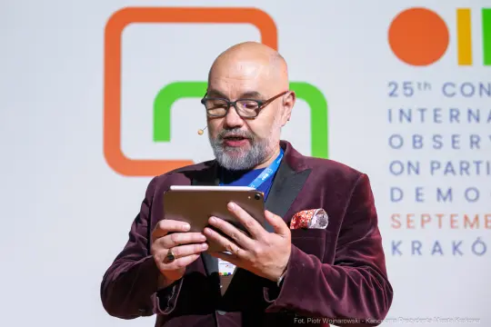 Mężczyzna w okularach trzyma tablet i przemawia na konferencji.