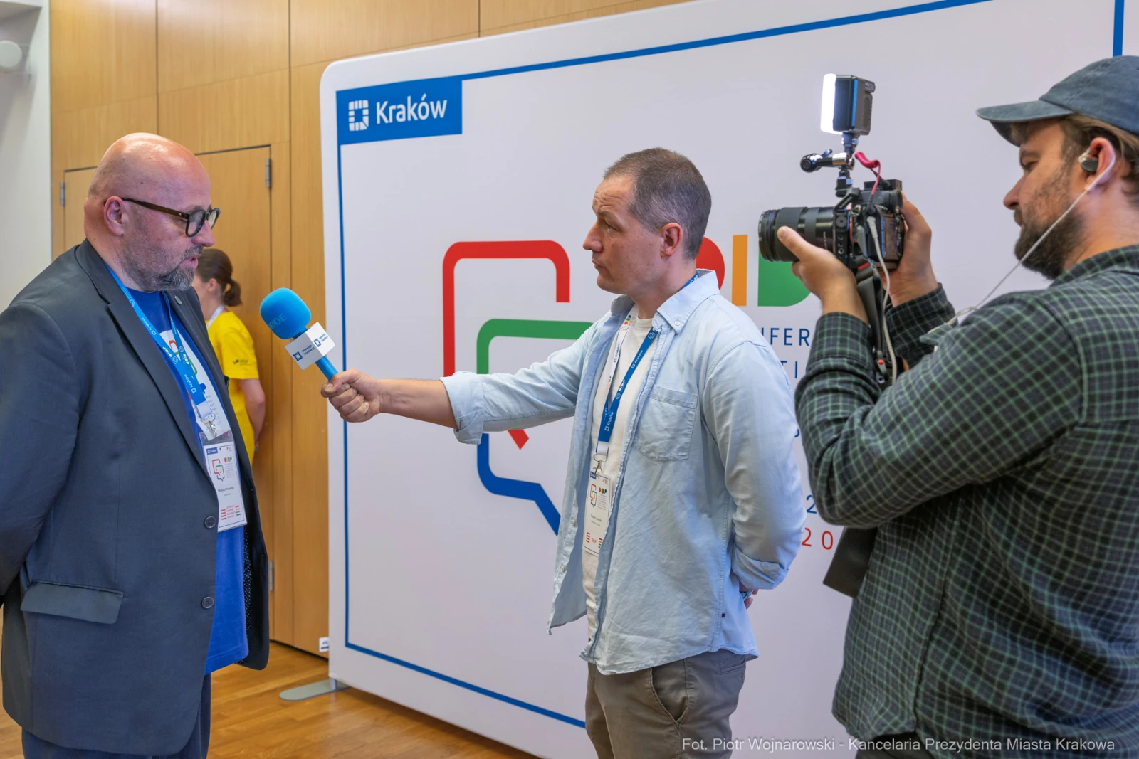 Wywiad z mężczyzną w garniturze, dziennikarz z mikrofonem i kamerą. Tło z logo Krakowa.  Autor: Piotr Wojnarowski