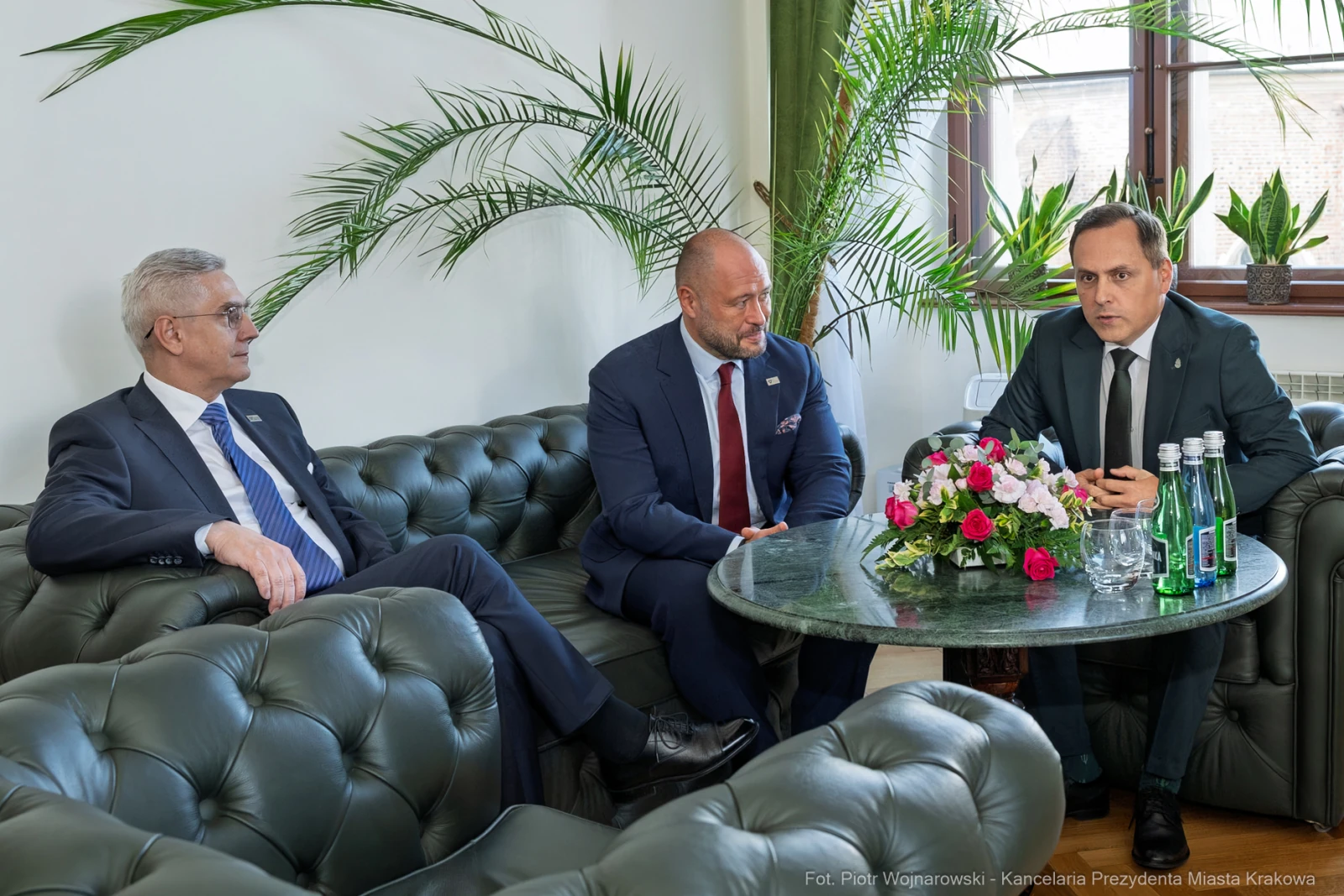 Trzech mężczyzn w garniturach siedzi na kanapie przy stole z kwiatami i wodą mineralną.  Autor: Piotr Wojnarowski