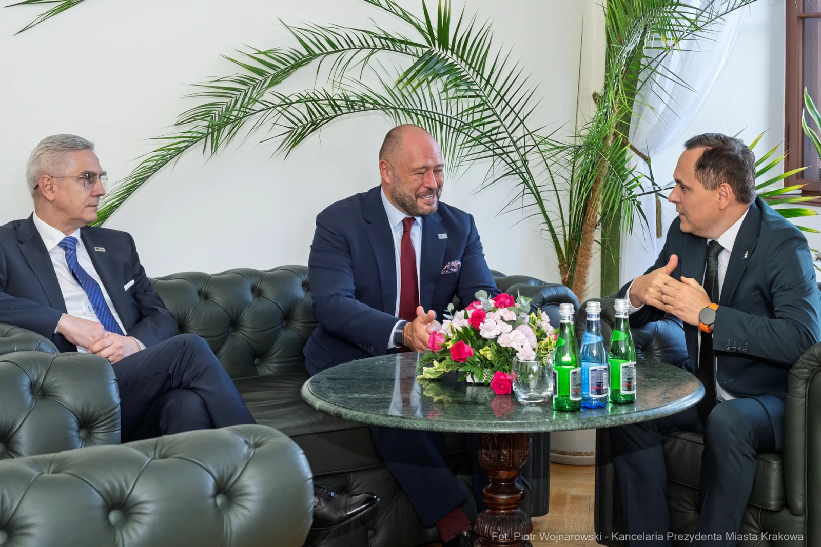 Spotkanie trzech mężczyzn w eleganckim wnętrzu z kwiatami i napojami na stole.  Autor: Piotr Wojnarowski