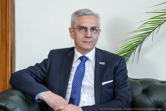Mężczyzna w garniturze siedzący na kanapie, z poważnym wyrazem twarzy.