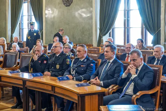 Grupa mężczyzn w garniturach i mundurach siedzi w sali obrad.