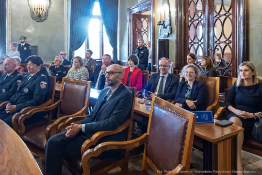 Spotkanie w sali obrad z uczestnikami w różnych strojach, w tym mundurach.